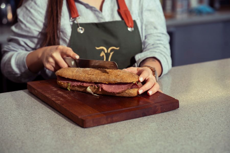 Smoky roast beef sandwich being sliced on a wooden cutting board